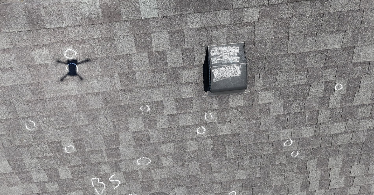 Detailed image of a roof vent surrounded by multiple chalk-marked hail damage spots during a roof inspection.