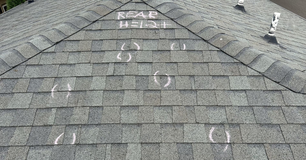 Close-up of roof shingles with chalk markings indicating areas of hail damage during a professional roof inspection.