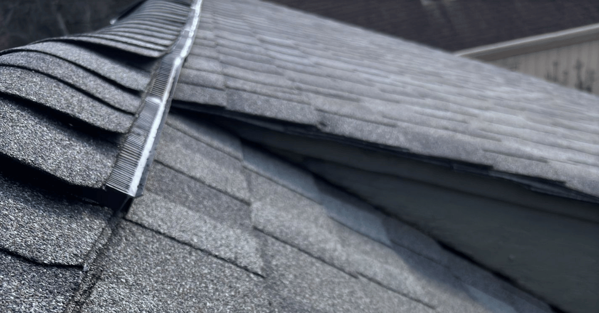 Close-up image of a shingle roof with significant structural damage and a ridge vent.