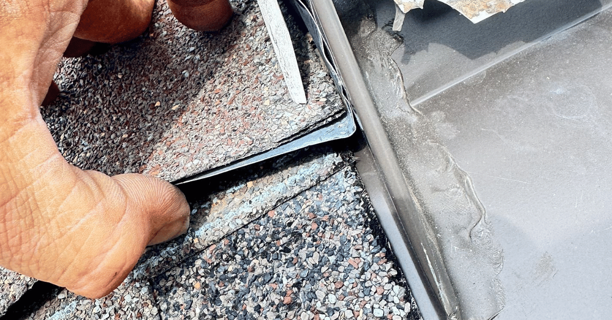 Metal flashing being lifted to reveal poor sealing and water intrusion, a common reason for roofing repair under most roofing warranties.