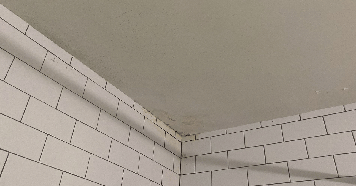 Water-stained bathroom ceiling beneath tiled walls, caused by a roof leak and inadequate flashing or ventilation.