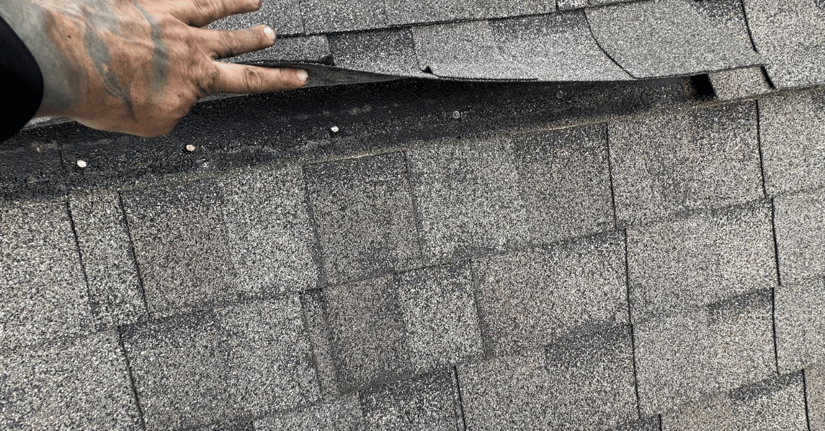 Roofing contractor lifting shingles to reveal multiple layers of old roofing materials, a common issue with roof overlays and layovers.
