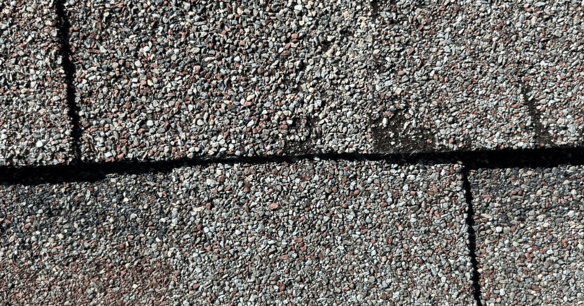 Close-up image showing worn asphalt shingles with granule loss, a common sign of aging roof materials and potential leak risk.