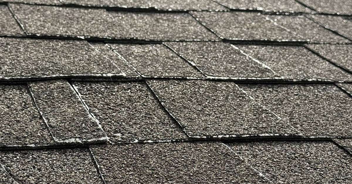 Roof shingles showing patchy discoloration due to granule loss and UV damage from the summer sun.