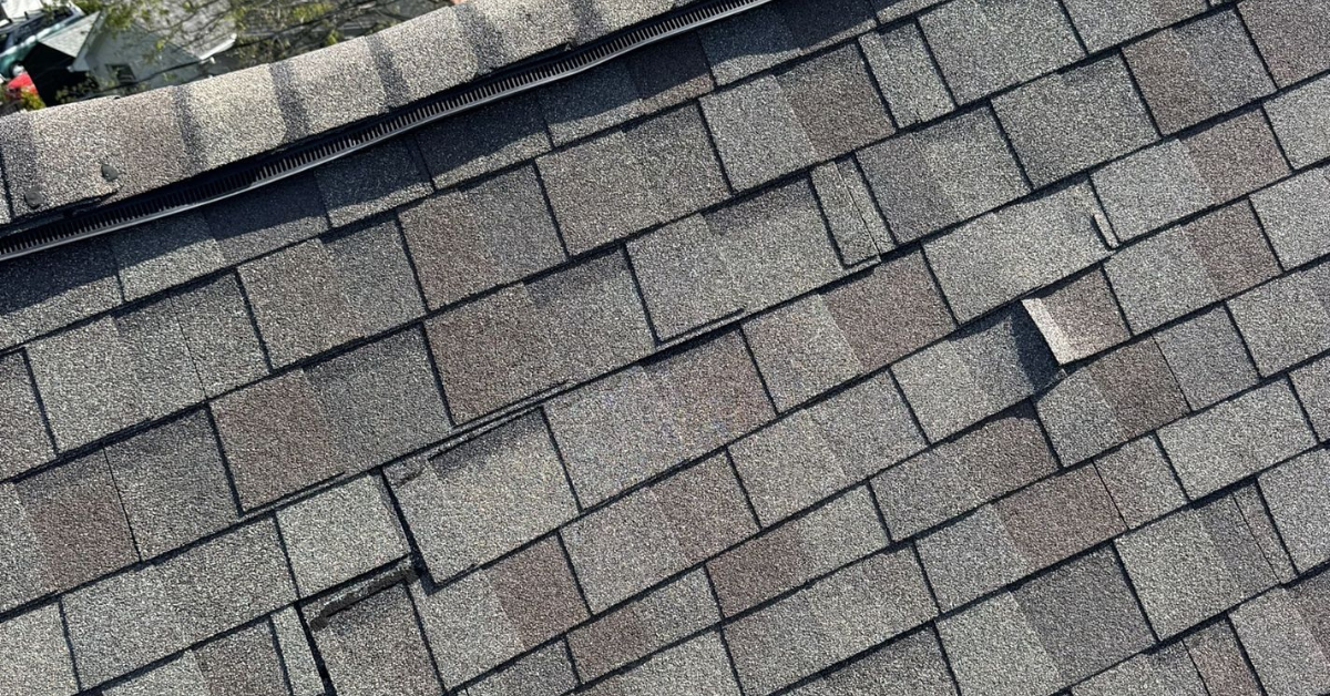 Shingles lifted and displaced by strong winds compromising roof integrity and increasing risk of water intrusion