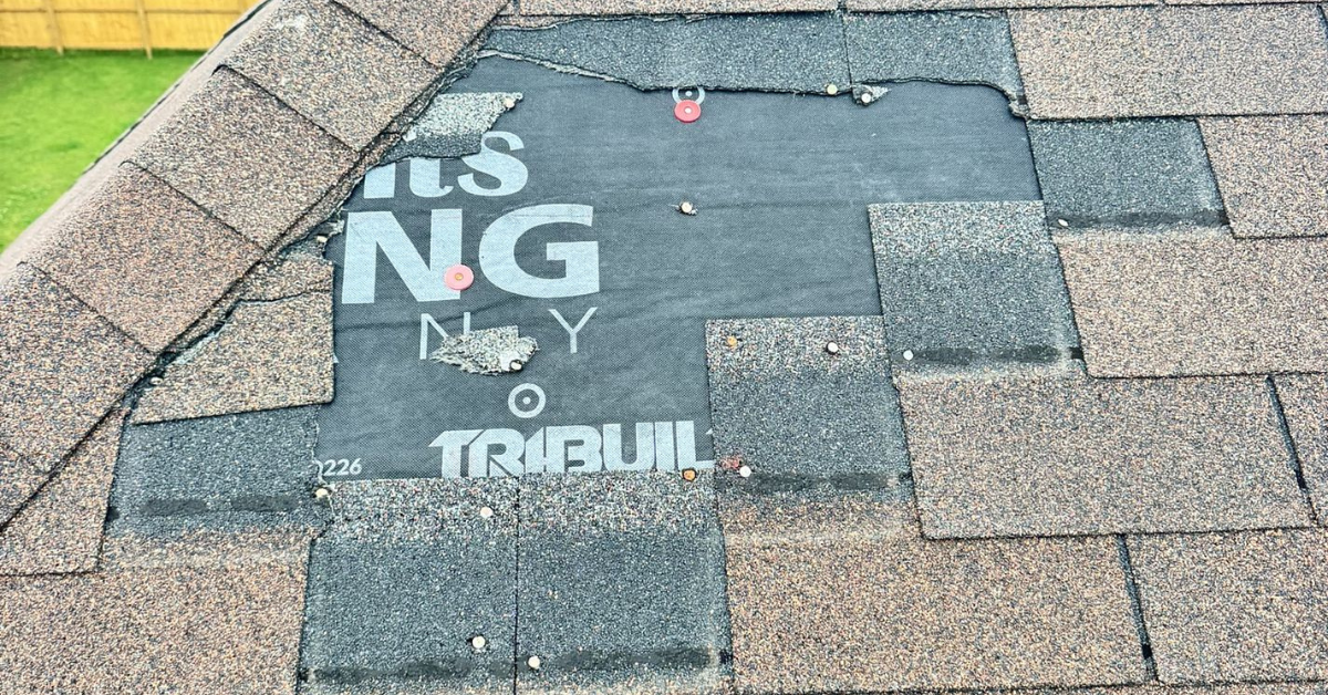 Wind-damaged roof showing missing shingles and exposed roofing underlayment after a Tennessee storm