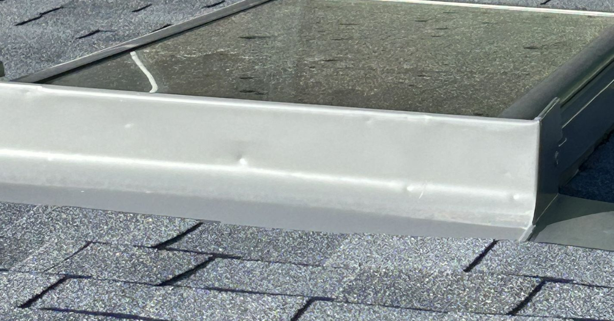 Metal frame of a skylight showing small hail dents, an indicator of possible roof or shingle damage nearby.