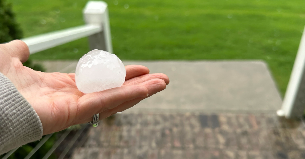 A hand holding a large hailstone, showing the size of hail that can cause significant hidden roof damage.