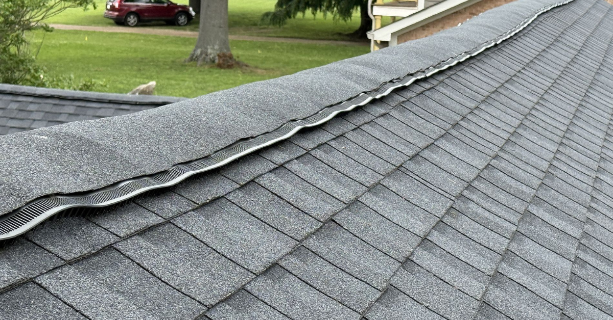 A ridge vent running along the peak of an asphalt roof, allowing hot attic air to escape and boosting energy efficiency during hot weather.