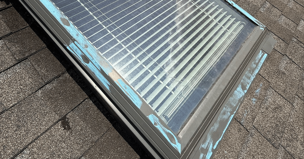 Skylight on asphalt shingle roof marked with chalk to identify potential water damage and accidental impact.