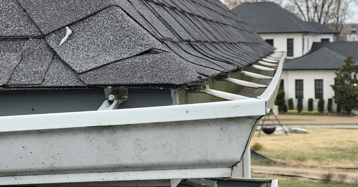 Detached and bent gutters with damaged shingle edges after a severe storm in the Nashville area