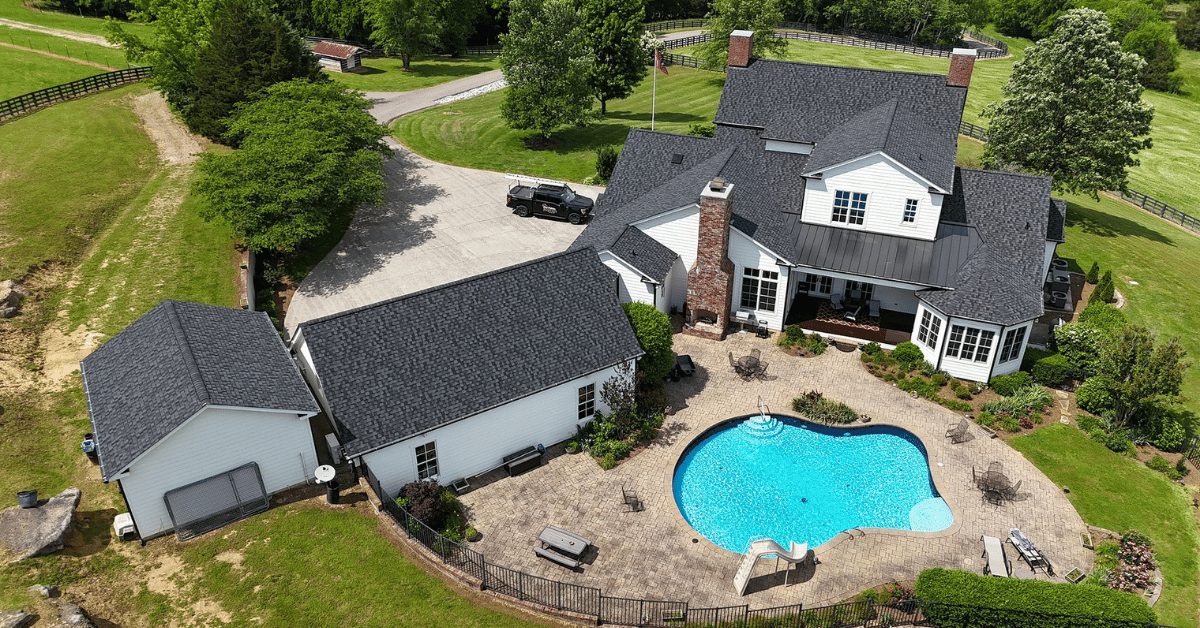 Completed roof replacement using black shingles with a clear view of the backyard, pool, and outbuildings.