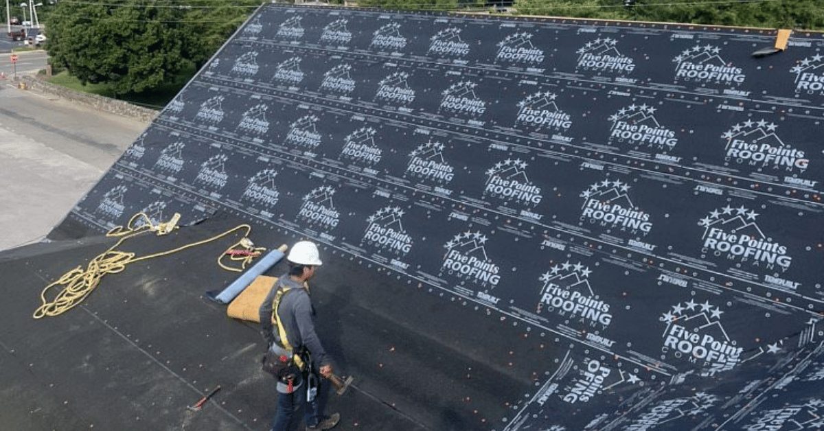 Roofer applying branded synthetic felt across steep roof section on new downtown Franklin office building.