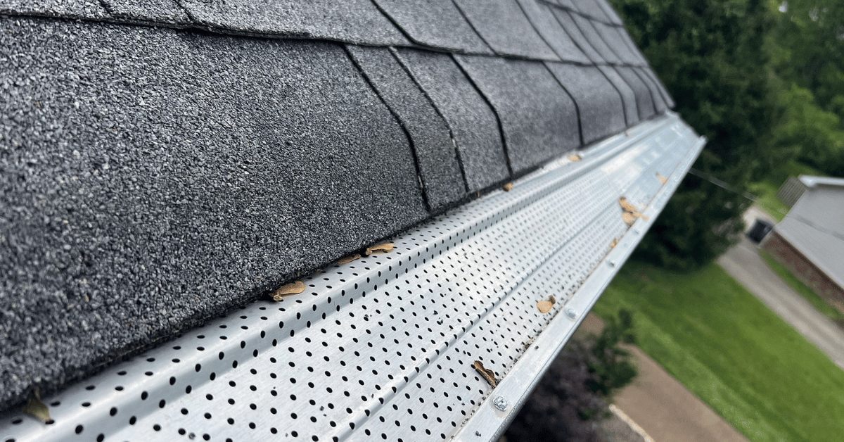 Close-up of roof shingles and a metal gutter guard installed to prevent leaf buildup and improve water drainage.
