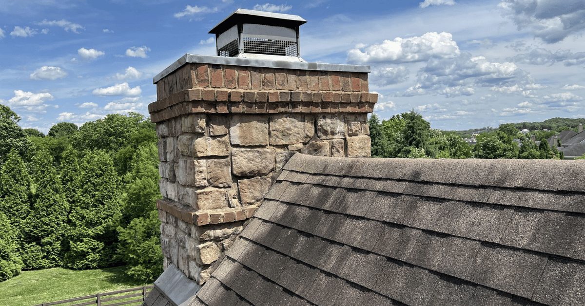Stone Chimney and Asphalt Shingles – College Grove Roof Inspection View of a stone chimney and aging asphalt shingles before roof replacement in College Grove, TN.