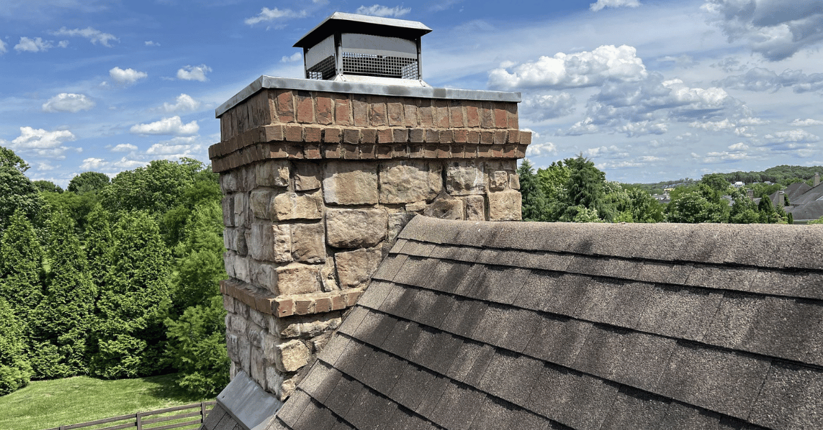 View of a stone chimney and aging asphalt shingles before roof replacement in College Grove, TN.