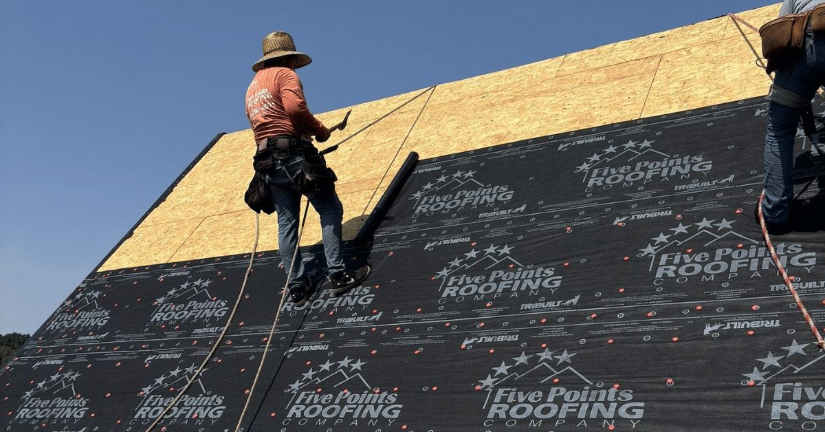 Roofer securing underlayment with Five Points Roofing branding visible, ensuring leak protection before shingle installation.