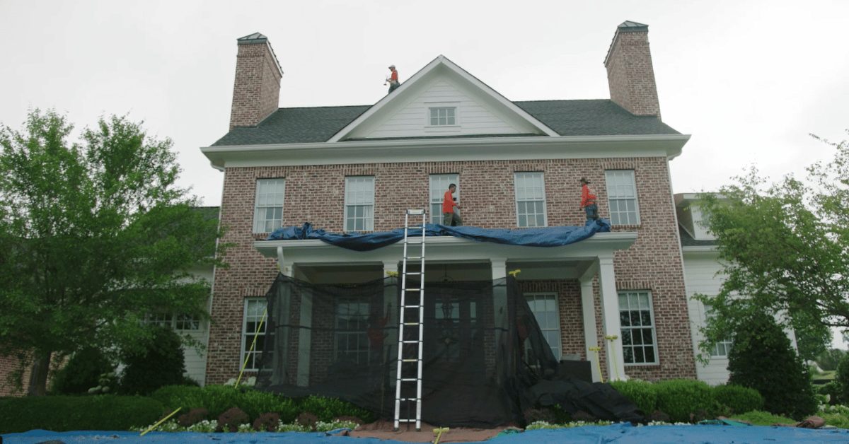 Roofing crew installs safety tarps and netting to protect the exterior and landscaping of a two-story brick home during roof replacement in Franklin, TN.