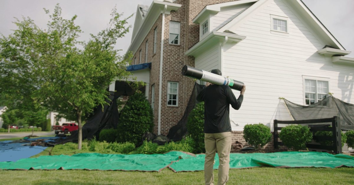 Roofer carrying roofing underlayment across a lawn covered with protective tarps to prevent damage during site preparation in Middle Tennessee.