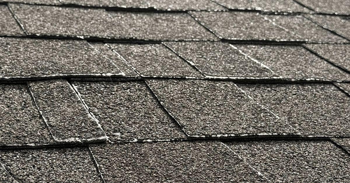 Asphalt roof shingles showing visible warping and lifting edges due to prolonged exposure to intense heat and UV rays.