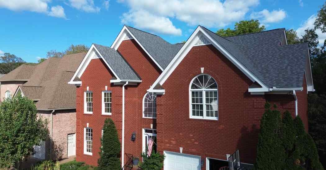A newly installed gray architectural shingle roof by Five Points Roofing on a red brick home under sunny skies.
