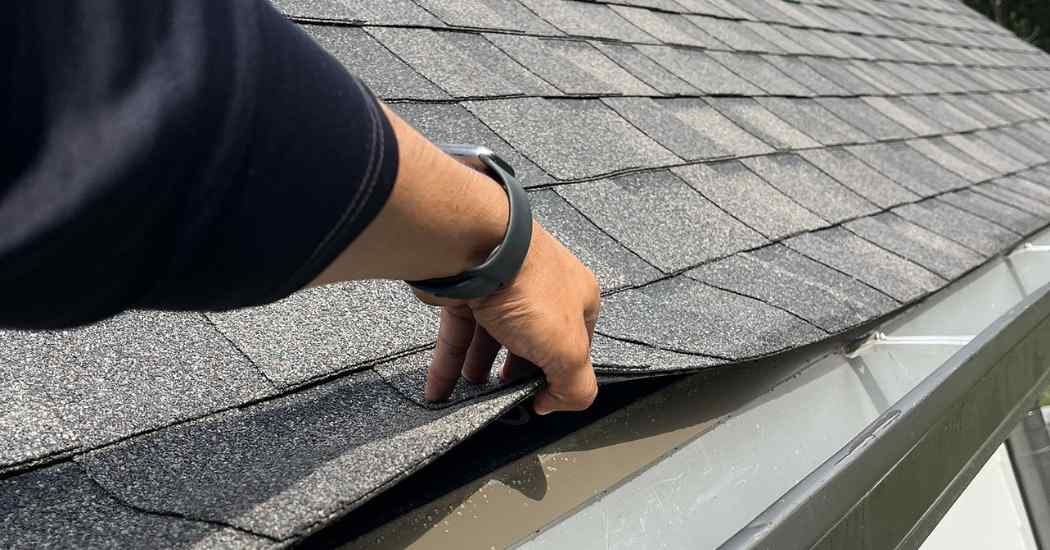 Roofer inspecting shingle lifting along the roof edge, a common early sign of moisture intrusion and the need for roof repairs.