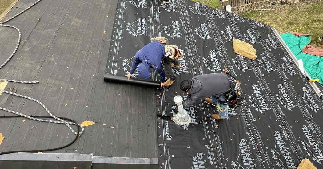Two roofers from Five Points Roofing laying synthetic underlayment and securing flashing to prep the roof deck for replacement.