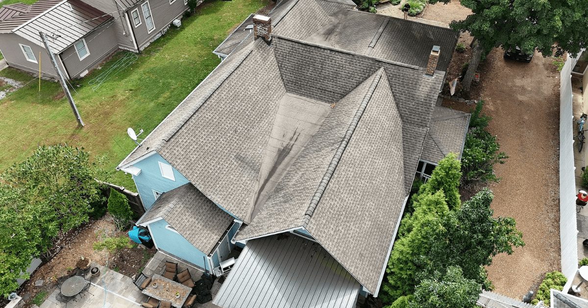 Aerial view of a home's asphalt shingle roof with dark stains and visible wear.