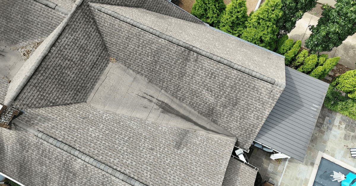 Aerial view of a house's roof showing dark stains and uneven shingle wear.
