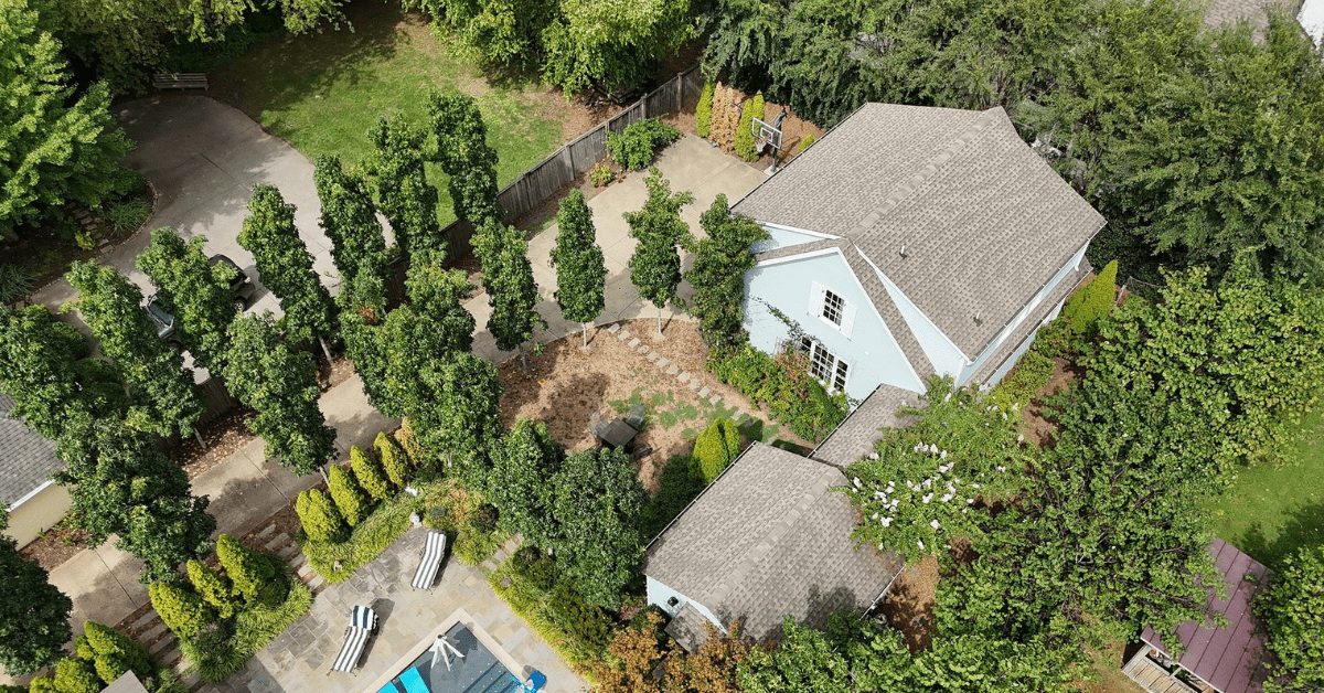 Aerial view of a home with an asphalt shingle roof surrounded by trees and a backyard.