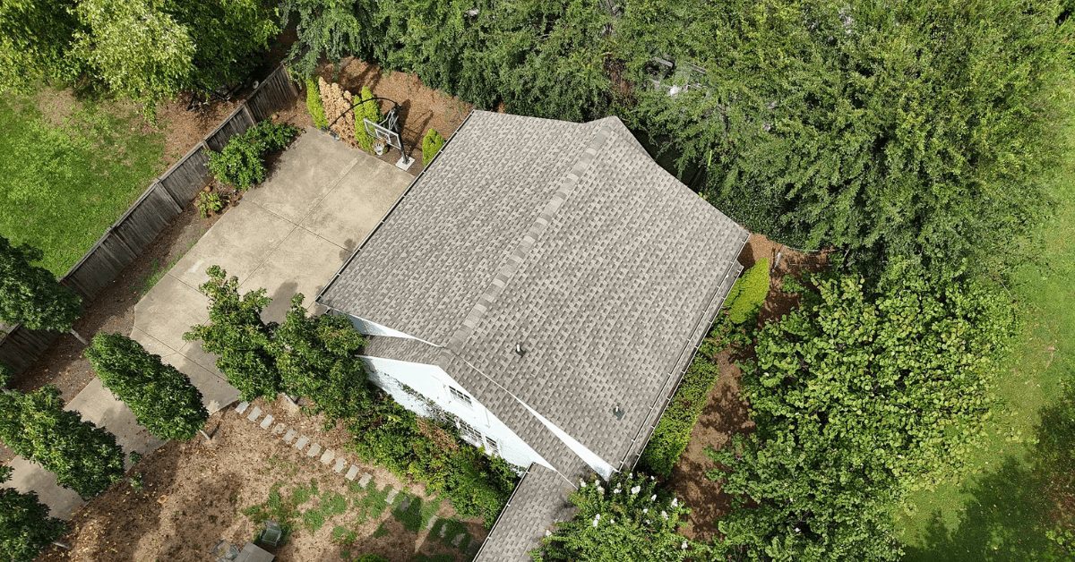 Aerial view of a residential home with an asphalt shingle roof surrounded by greenery.