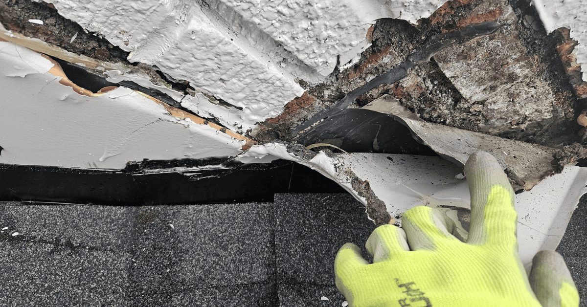 A close-up of a brick chimney with deteriorating mortar and surrounding roof damage.