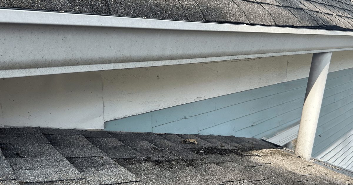 Close-up of a roof edge with white gutters and visible cracks in the house's siding.