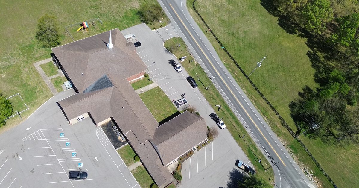 West Harpeth Church Roof Replacement — Franklin, Tennessee Aerial drone view of a brick church with a completed brown asphalt shingle roof, white steeple, and surrounding parking lot in Franklin, TN