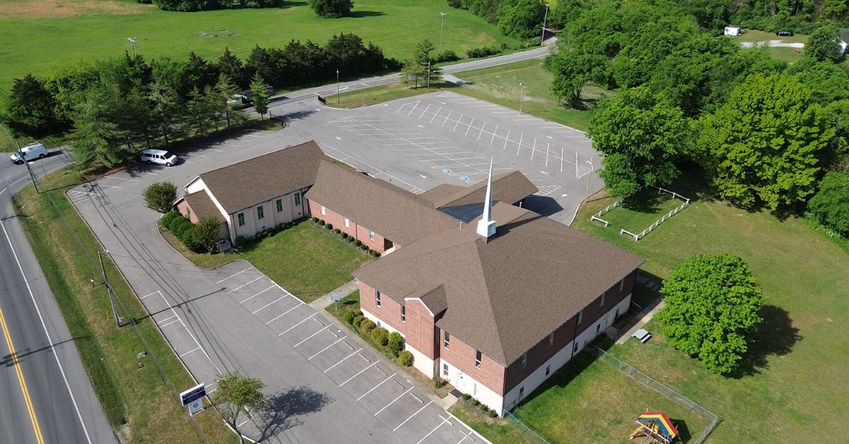 Aerial After View — Church Commercial Reroof, Franklin, TN Wide aerial drone view of a completed multi-building church campus with new brown asphalt shingle roofs and white steeple in Franklin, Tennessee