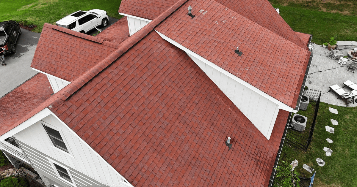 Aerial view of a red shingle roof with multiple dormers, a work truck, and SUV parked in the driveway