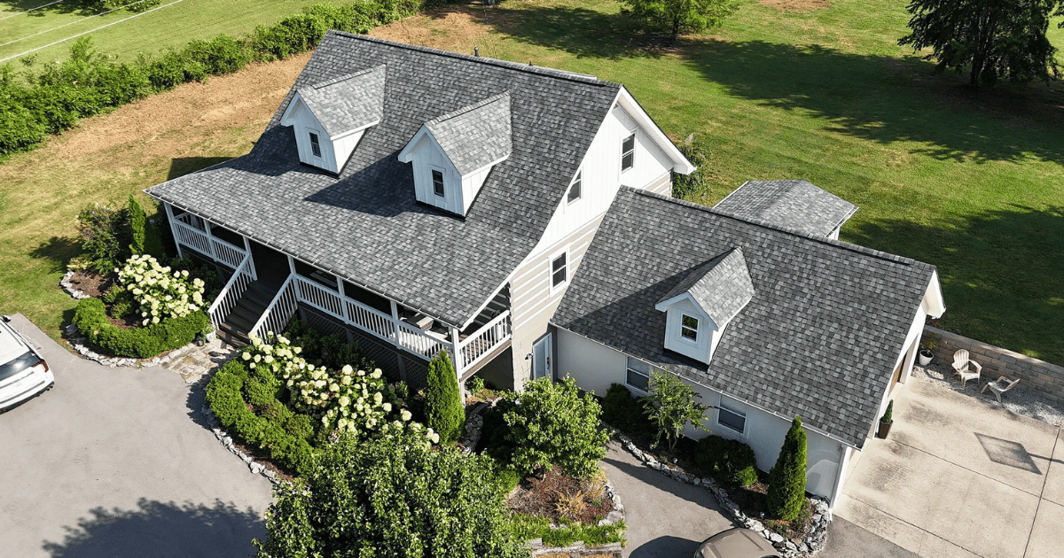 Aerial close-up of new charcoal gray shingles on hip roof sections and dormers with a patio below