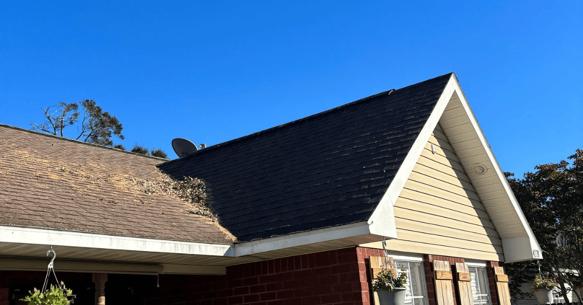 Brick ranch home with leaves and limbs piled on brown asphalt shingles next to a darker shingle section