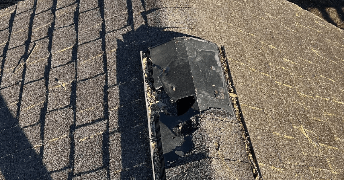 Close-up of a cracked and crushed black ridge vent on a weathered asphalt shingle roof